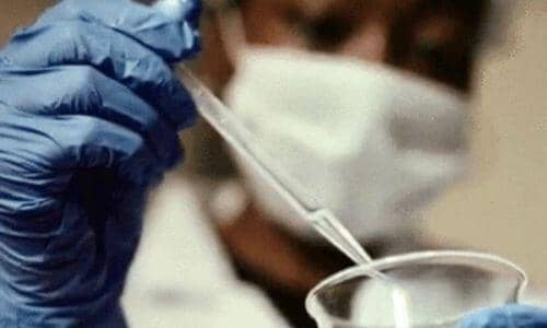 close up of a black worker wearing gloves and a mask using a pipette 