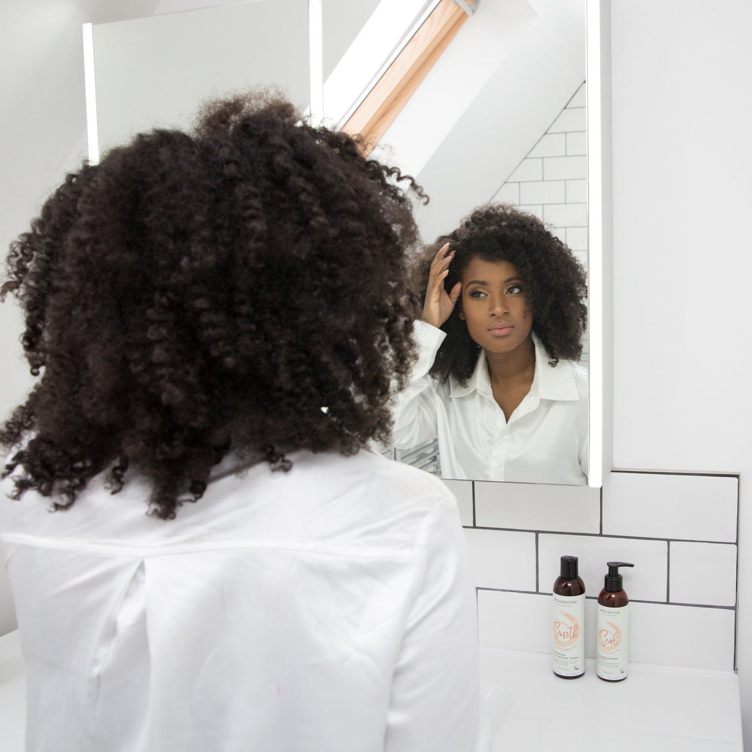 Afrocenchix Blog posts Everything you need to know about afro hair loss: Young black black woman wearing white looking in mirror touching hair