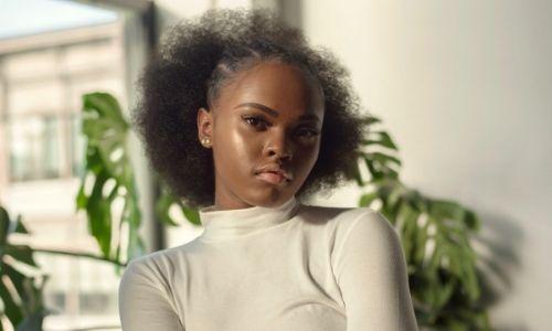 Afrocenchix blog post featured image - What causes split ends - young black woman with natural hair wearing white polo neck top with arms crossed