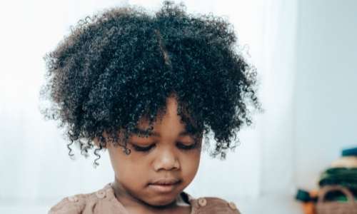 Black child with afro hair looking down- Child Q challenging hair discrimination in schools Afrocenchix article