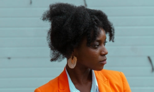 Heat Damaged Hair: Black woman with afro hair wearing an orange blazer looking the right 