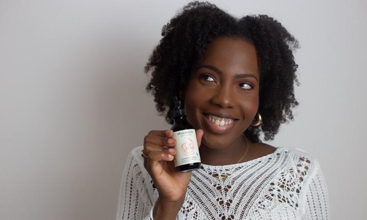 How to Stop an Itchy Itchy Scalp: Smiling black woman holding Soothe Afrocenchix scalp oil