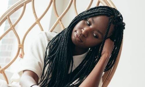 Dandruff vs dry scalp Afrocenchix article - young black woman with braids sitting on a wicker chair looking concerned