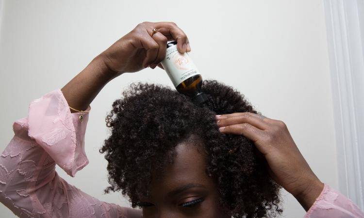 Why is my scalp so itchy? Close-up of black woman applying Afrocenchix oil to scalp
