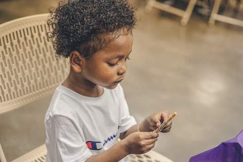 Young black girl with short curly hair looking down and holding and pen