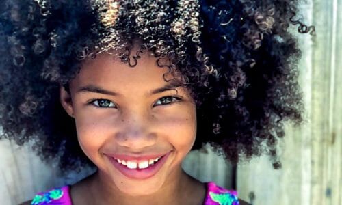 Afrocenchix article - why is my childs hair so dry - smiling black dad holding his daughter above him in a park