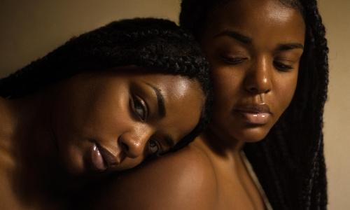 A beautiful black woman leaning on another black woman's shoulder