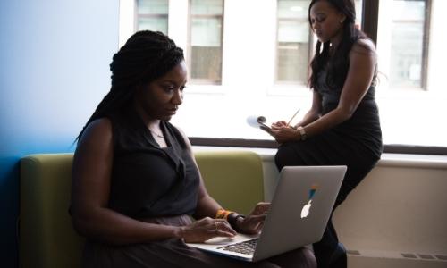 Two black women with laptops and phones working