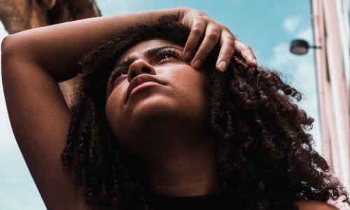 Hair loss alopecia: Black woman holding her curly natural hair and head looking up